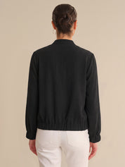 Person wearing a black jacket and white pants on a beige background