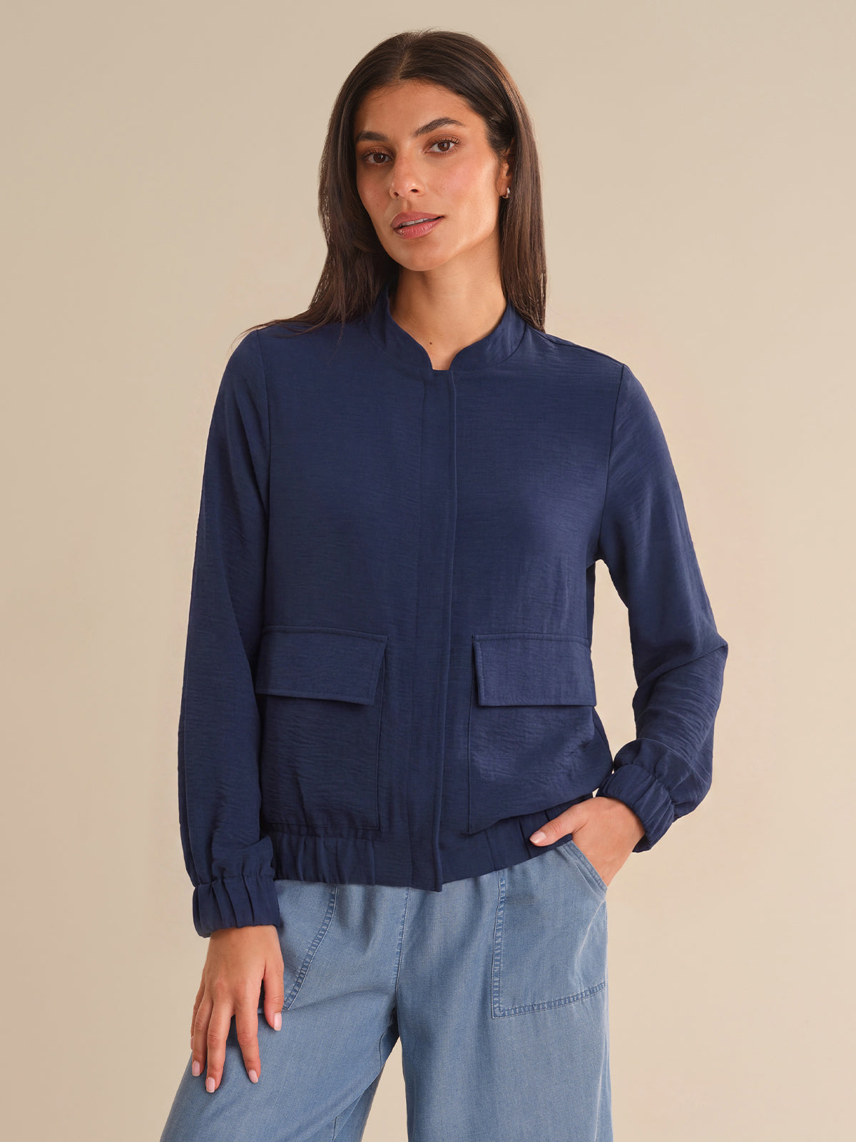Woman wearing a navy blue bomber jacket and light blue pants against a beige background
