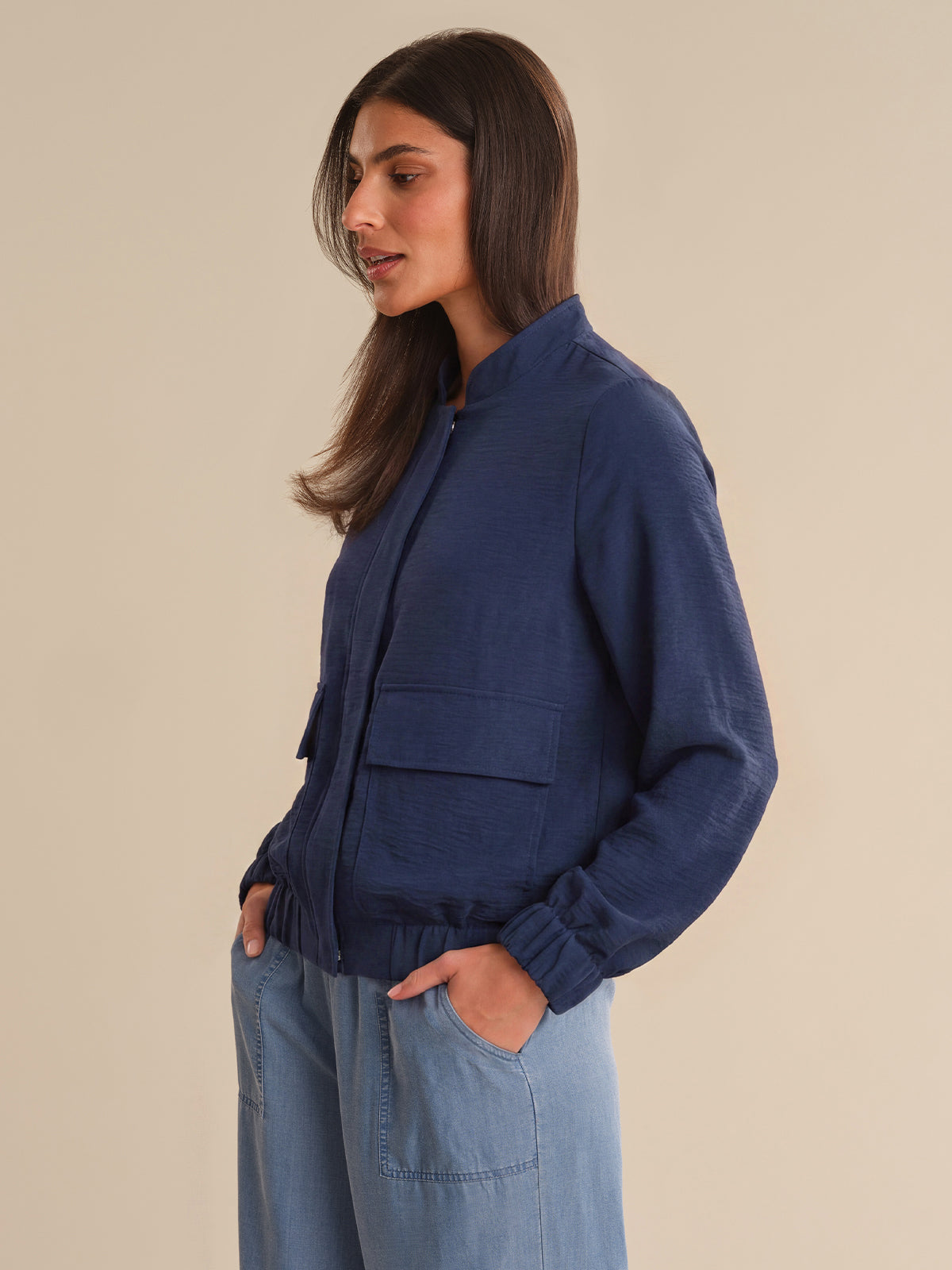 Woman wearing a blue jacket and light blue pants against a beige background