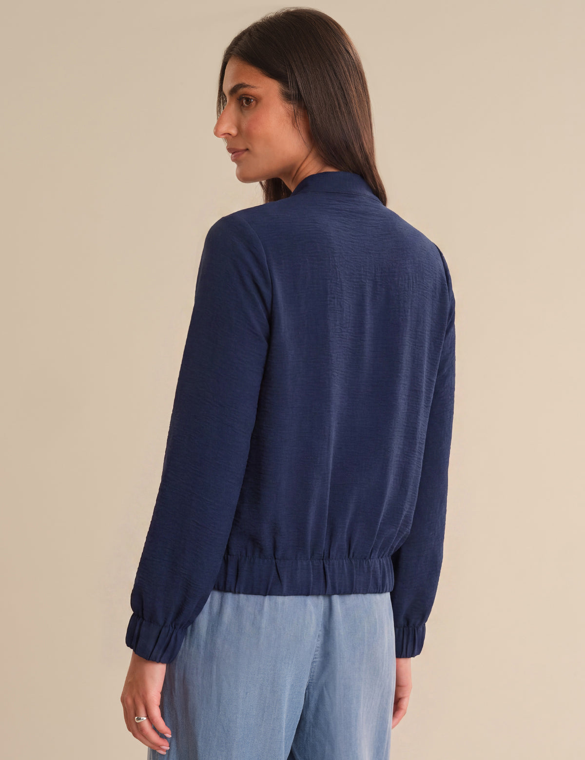 Woman wearing a navy blue sweater and light blue pants on a beige background