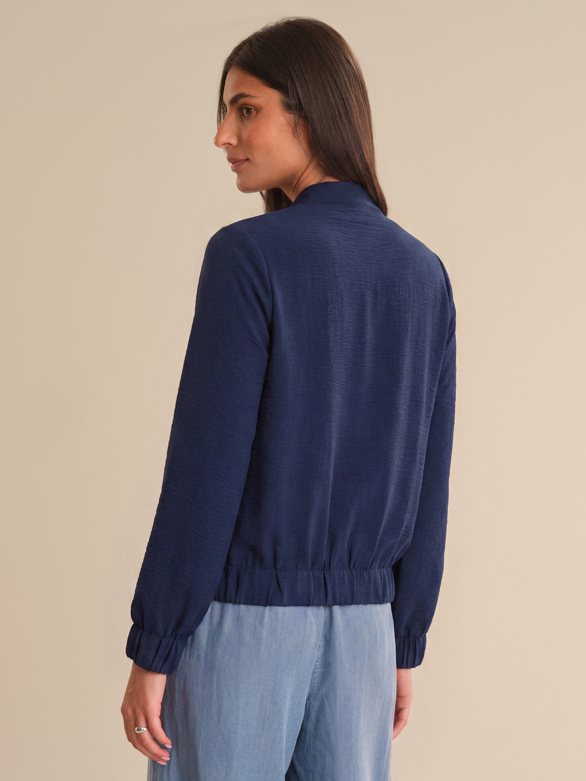 Woman wearing a navy blue sweater and light blue pants on a beige background