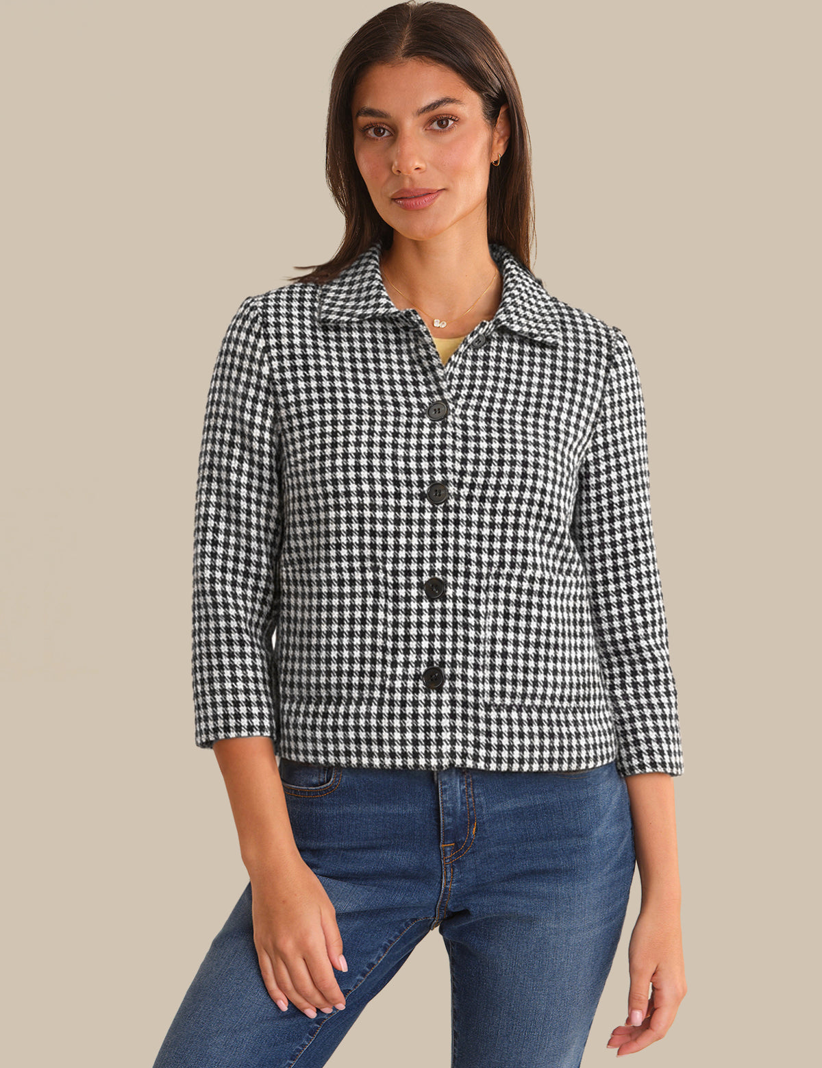 Woman wearing a black and white checkered jacket and blue jeans on a beige background