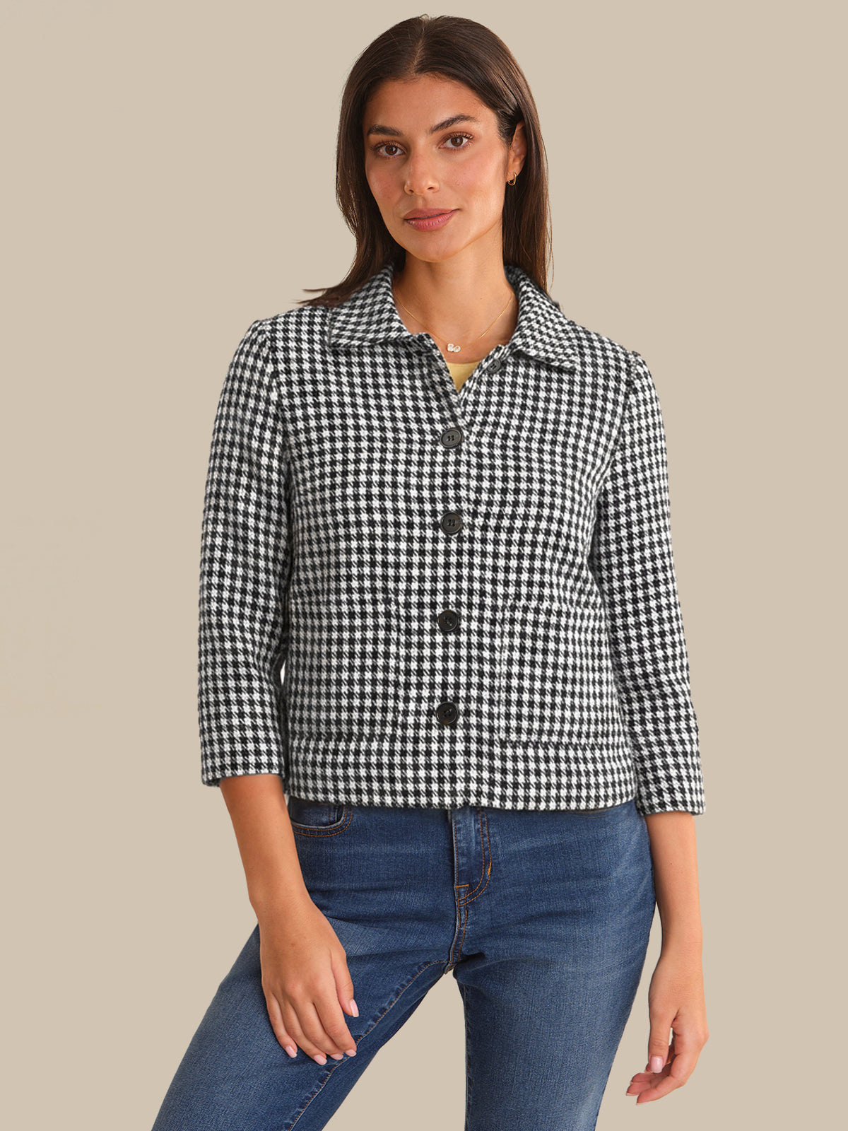 Woman wearing a black and white checkered jacket and blue jeans on a beige background