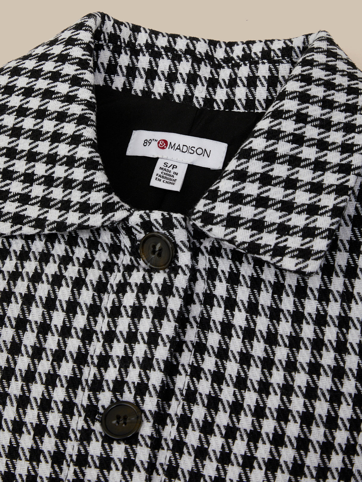 Close-up of a houndstooth patterned coat with a brand label.