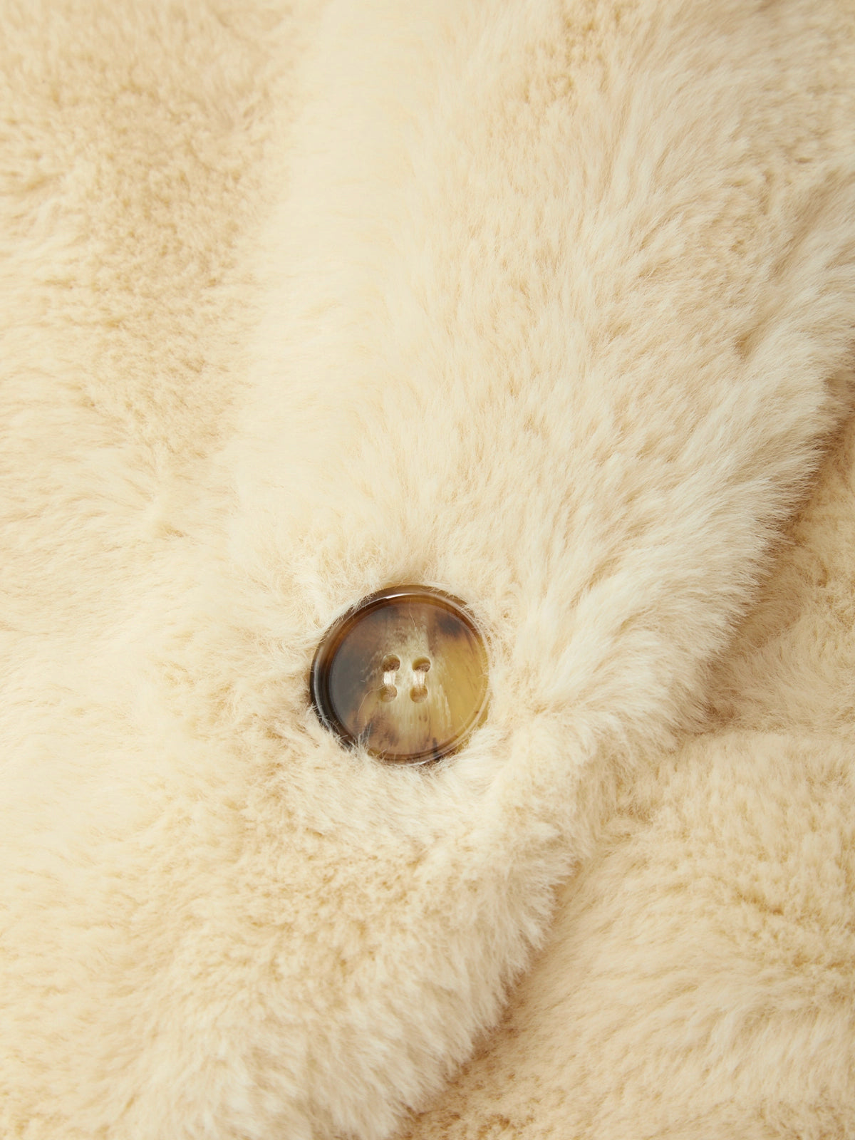 Close-up of a cream-colored fluffy faux fur garment featuring a single brown tortoiseshell button.