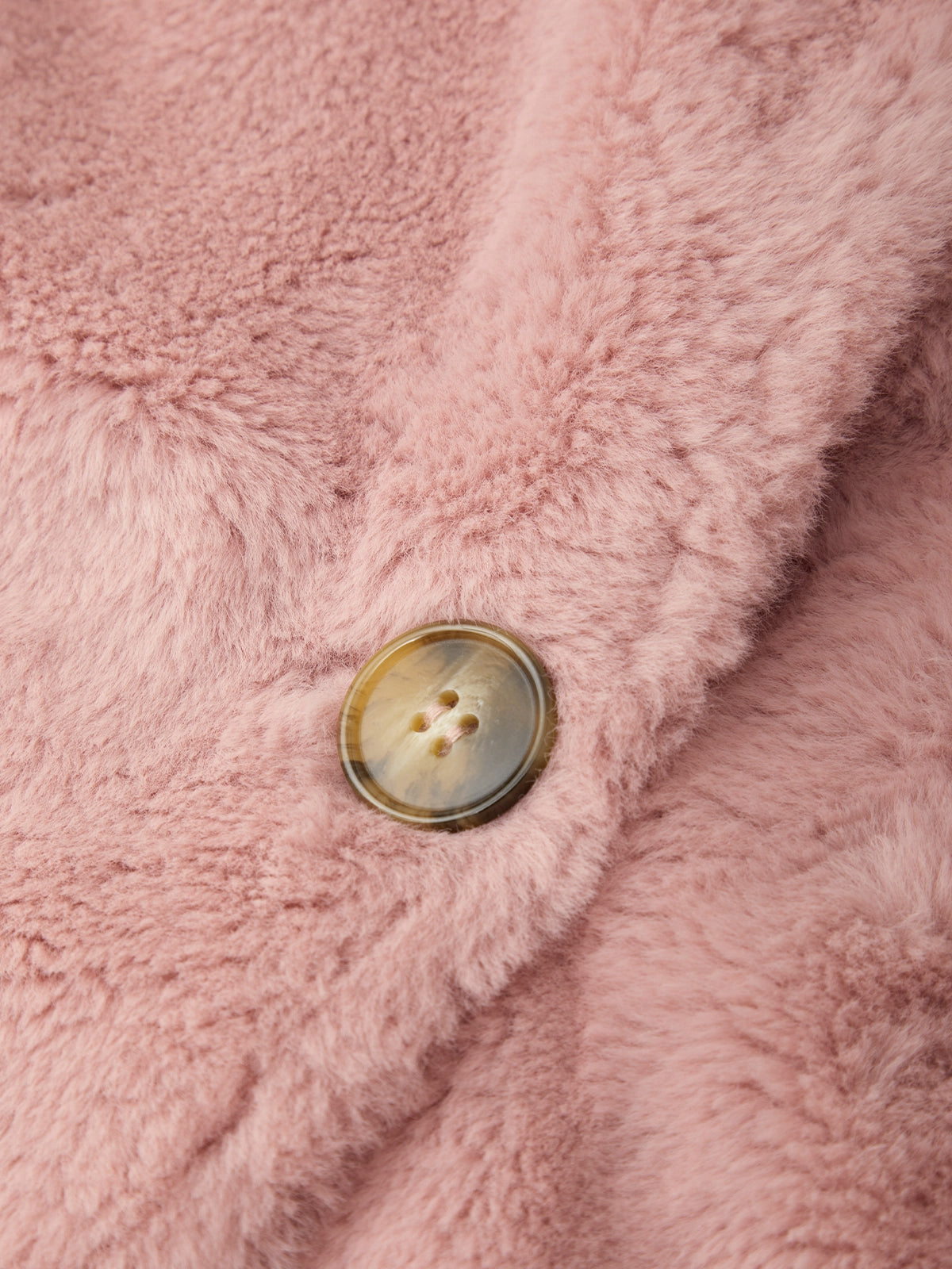 Close-up of a dusty pink faux fur or sherpa fabric with a single round brown button on a fold.
