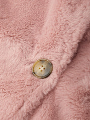Close-up of a dusty pink faux fur or sherpa fabric with a single round brown button on a fold.