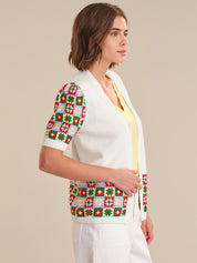 Woman wearing a white cardigan with colorful geometric patterns on sleeves against a beige background