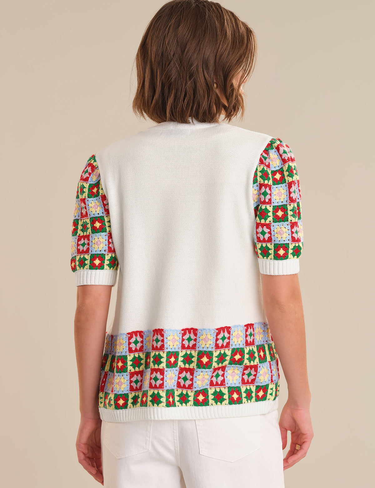 Person wearing a white sweater with colorful geometric patterns on a beige background