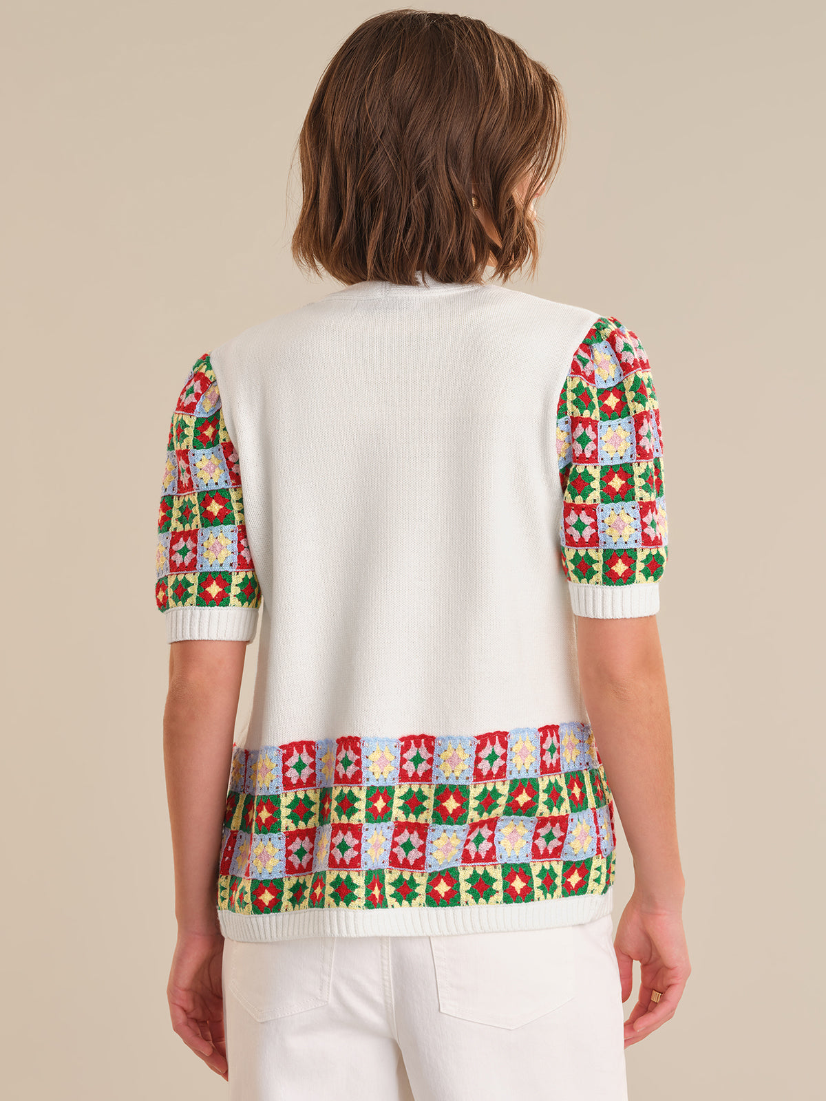 Person wearing a white sweater with colorful geometric patterns on a beige background