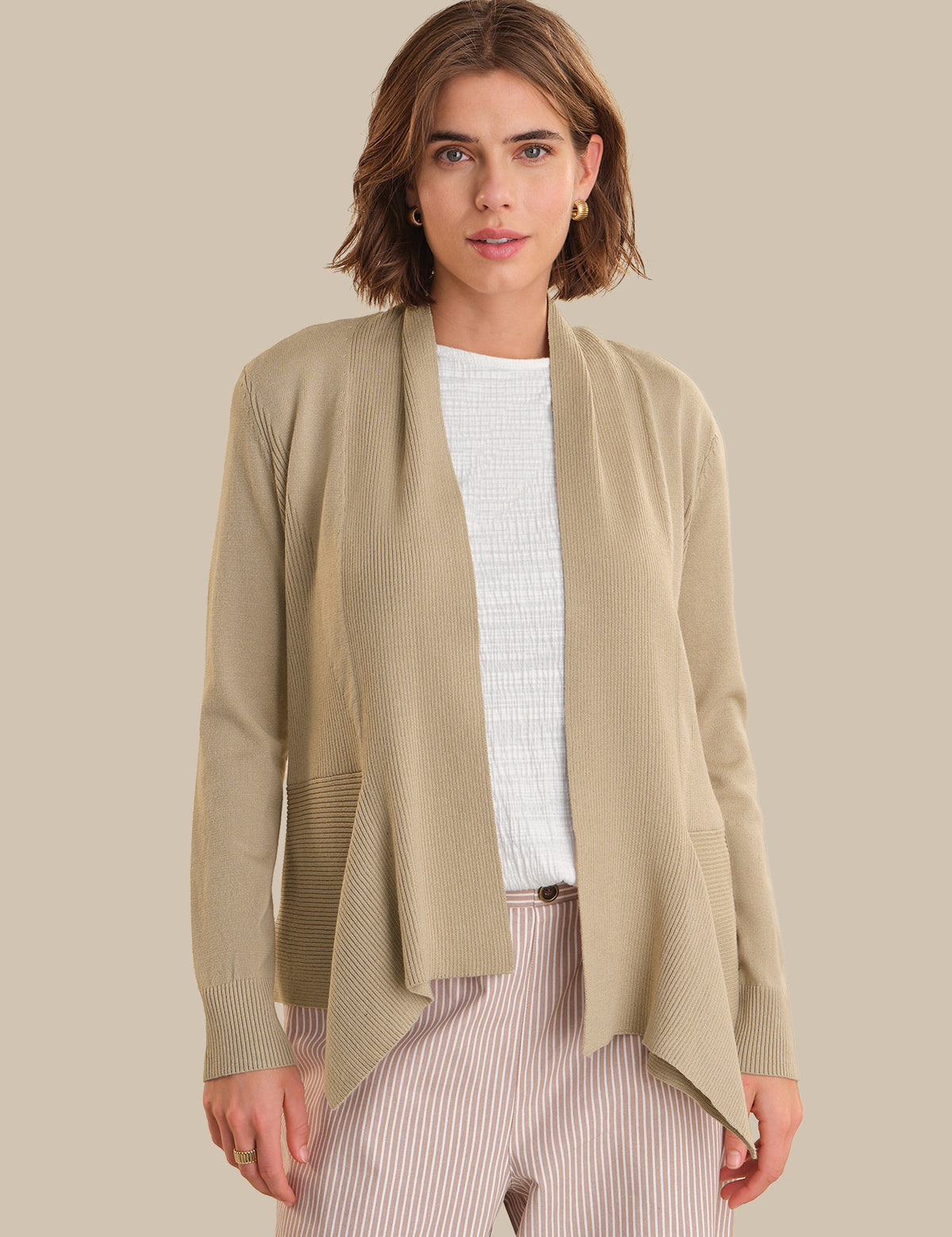 Woman wearing a beige cardigan over a white top and striped pants on a beige background