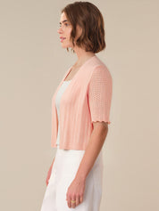 Woman wearing a light pink knitted cardigan over a white dress on a beige background