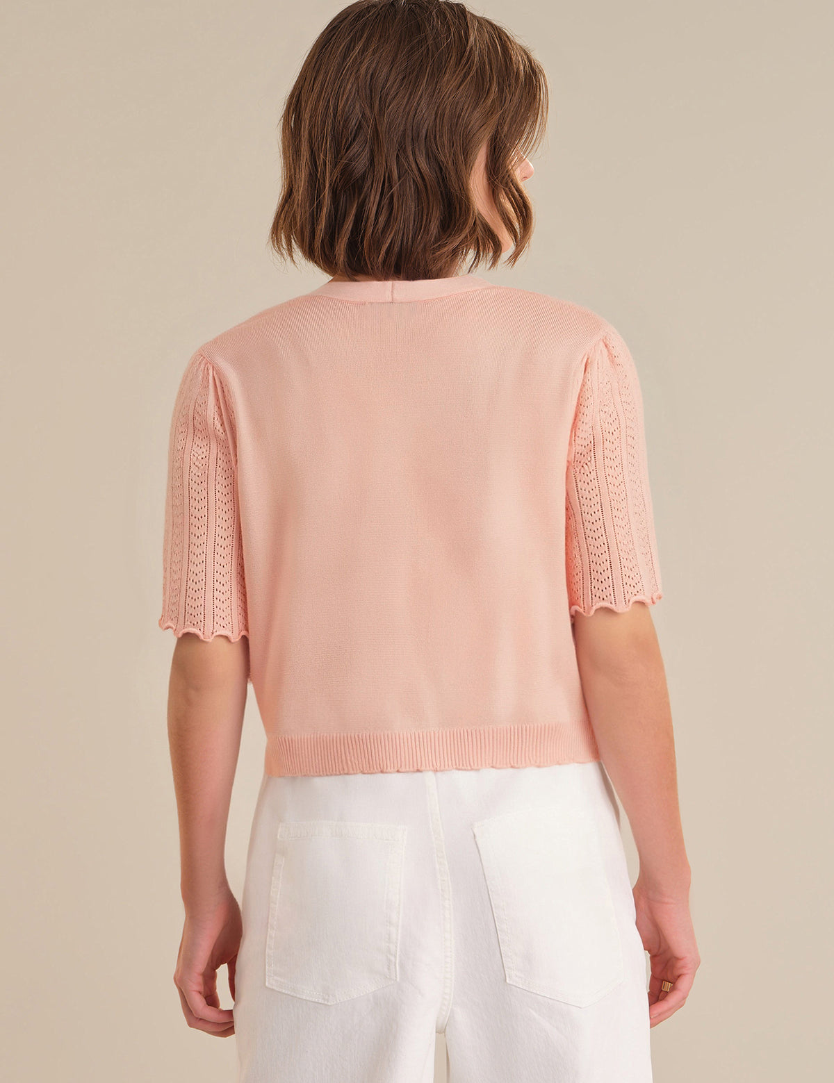 Person wearing a light pink sweater with short sleeves and white pants on a beige background