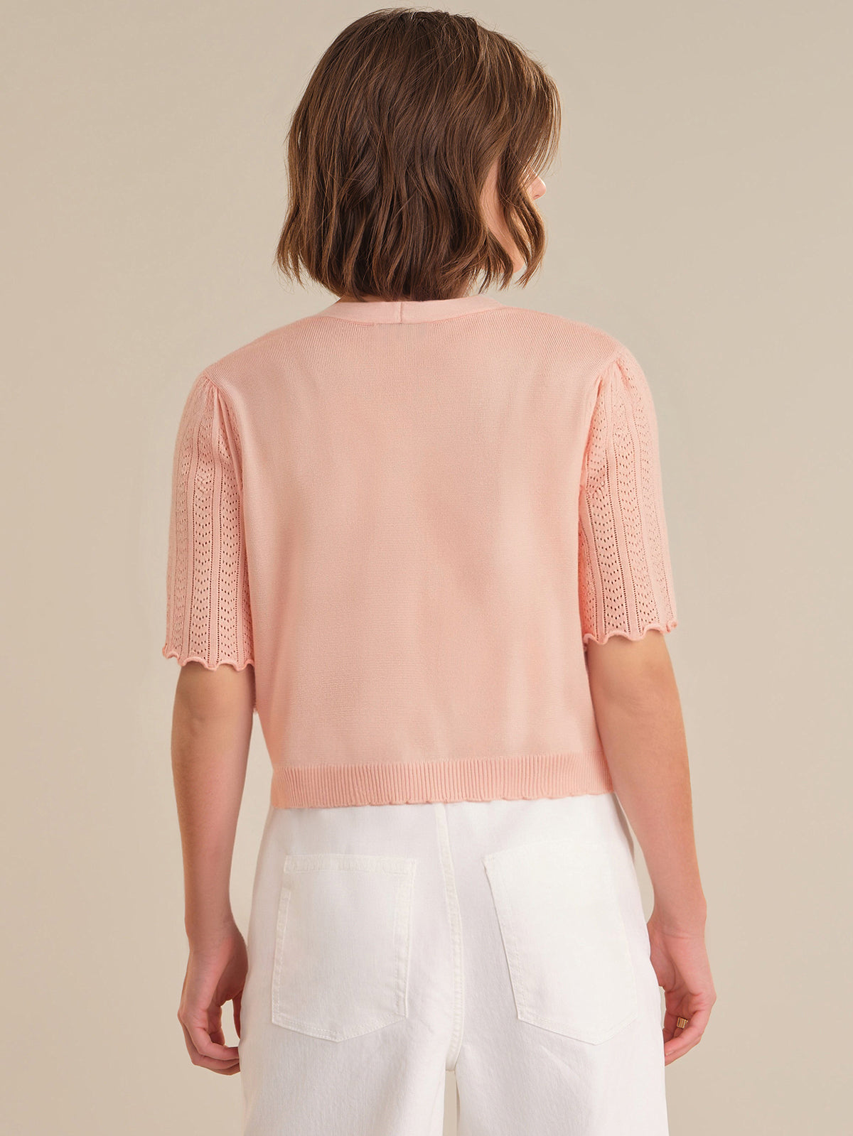 Person wearing a light pink sweater with short sleeves and white pants on a beige background