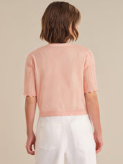 Person wearing a light pink sweater with short sleeves and white pants on a beige background