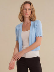Woman wearing a light blue cardigan over a white top and black pants on a beige background