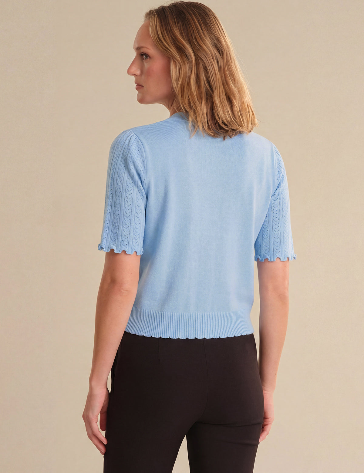 Woman wearing a light blue knitted top against a beige background