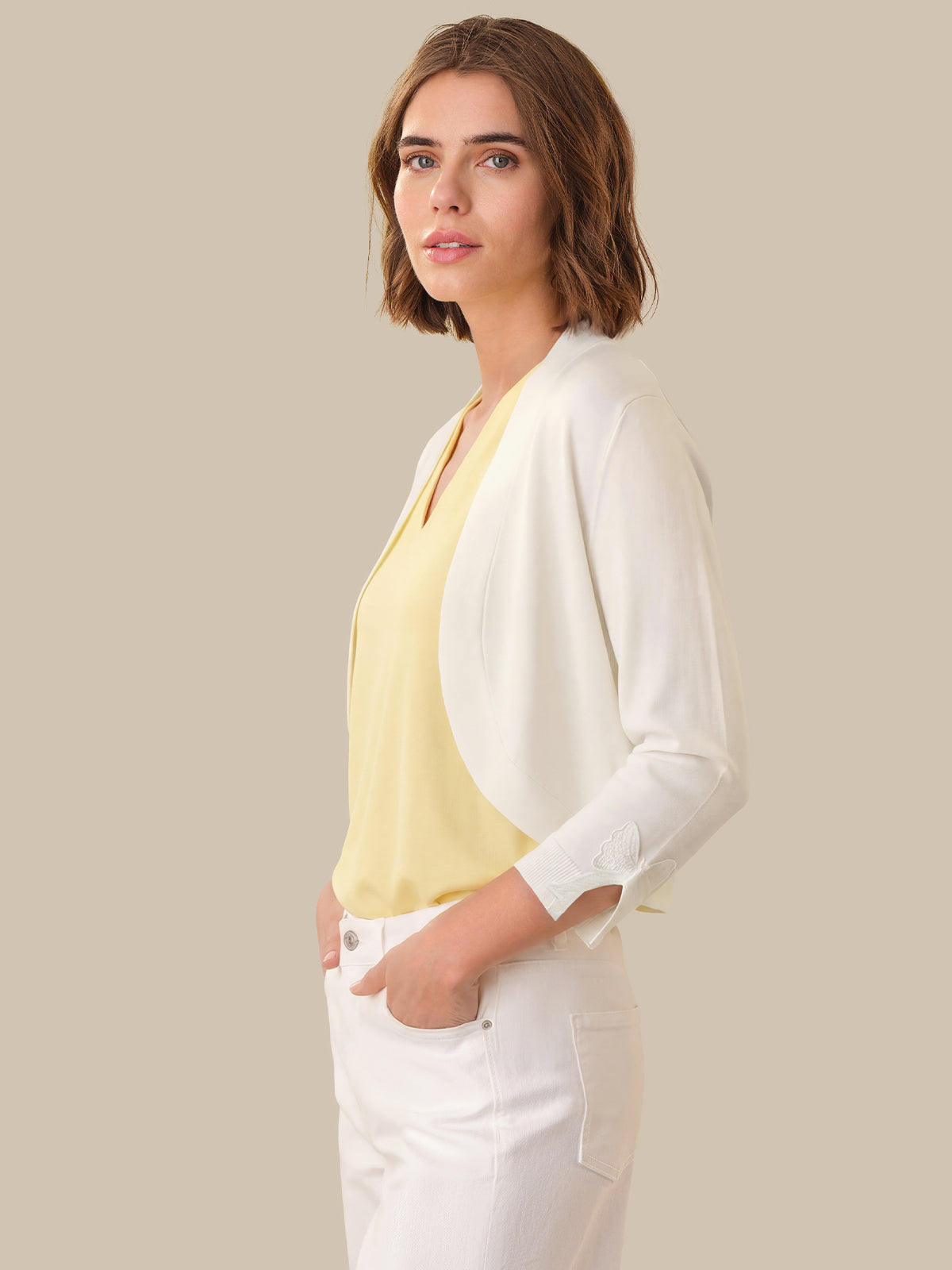 Woman wearing a light yellow top and white cardigan against a beige background