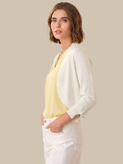 Woman wearing a light yellow top and white cardigan against a beige background