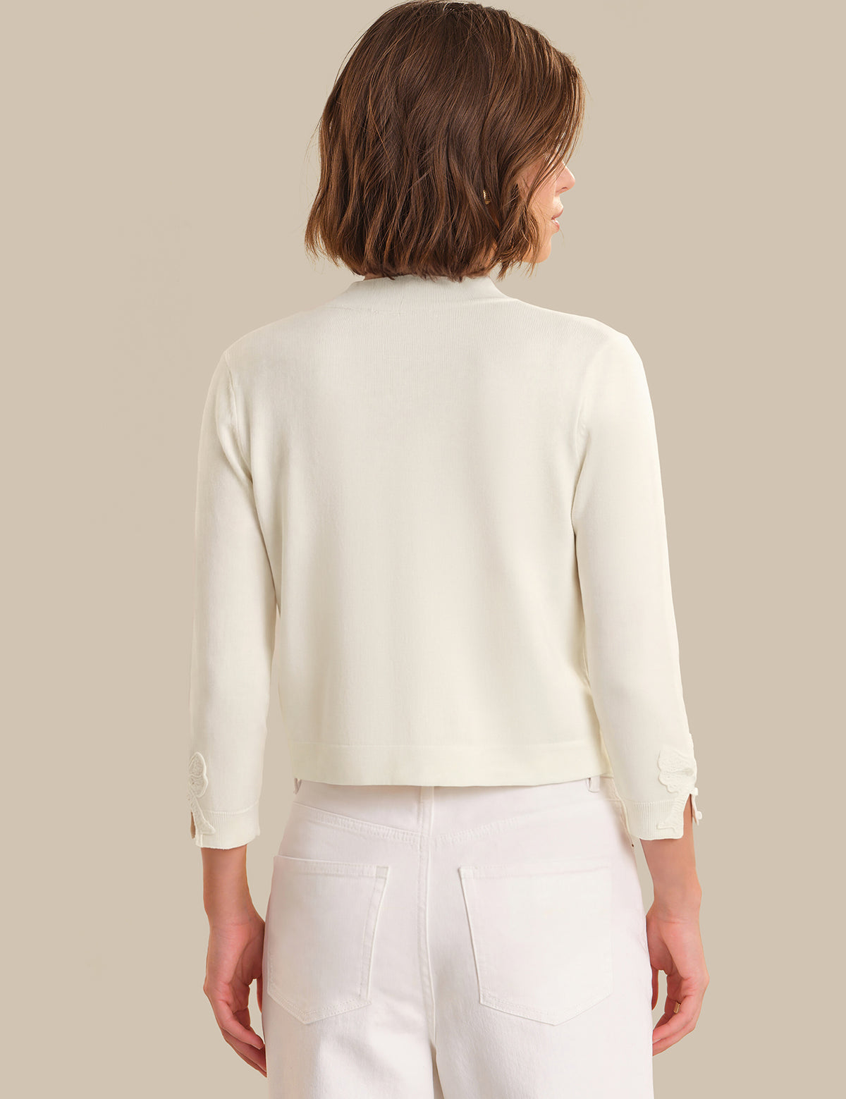 Woman wearing a light-colored cardigan over a white top and pants on a beige background