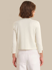 Woman wearing a light-colored cardigan over a white top and pants on a beige background
