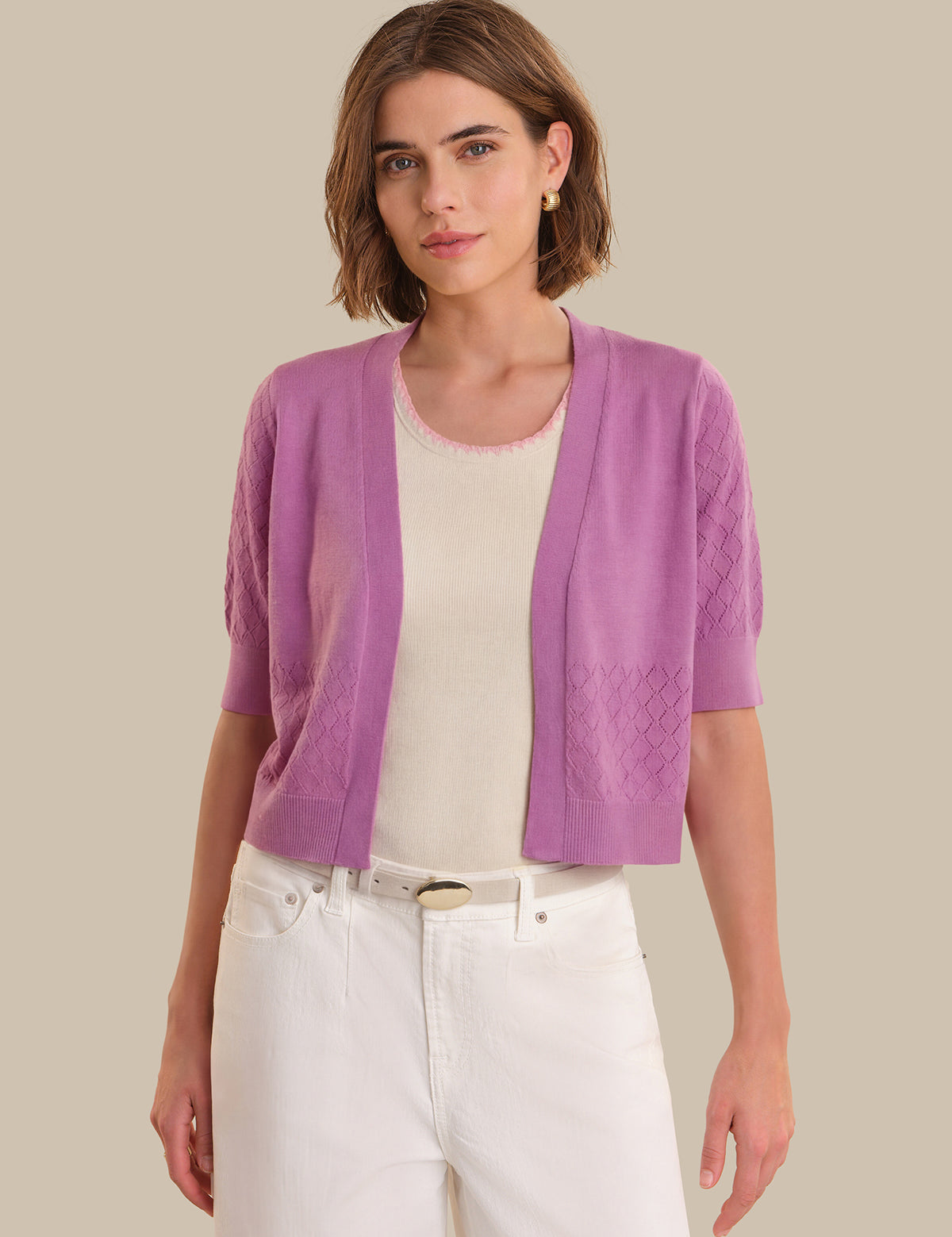 Woman wearing a purple cardigan over a white shirt and pants on a beige background