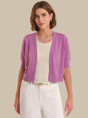 Woman wearing a purple cardigan over a white shirt and pants on a beige background