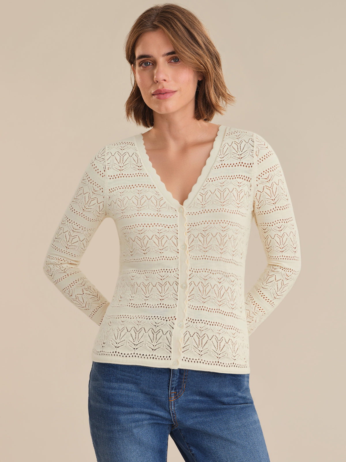 Woman wearing a light-colored lace cardigan over a blue top against a beige background