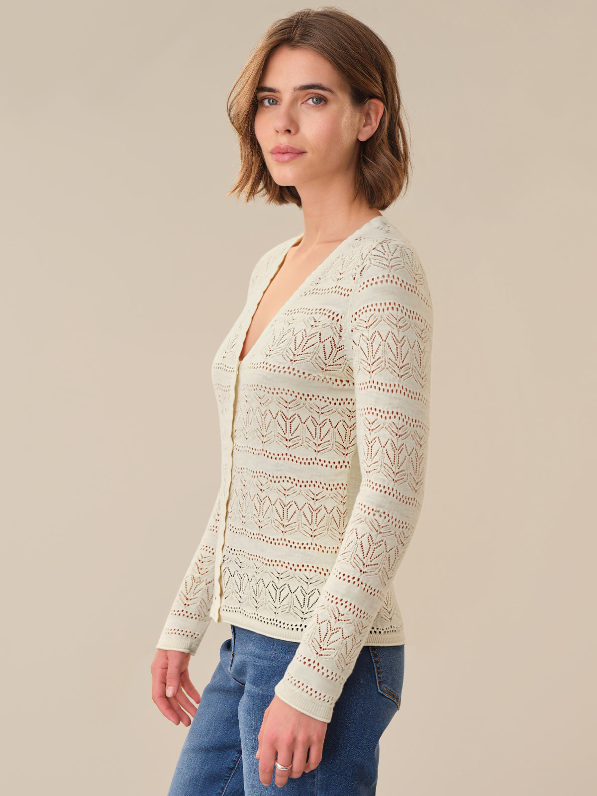 Woman wearing a cream lace cardigan against a beige background