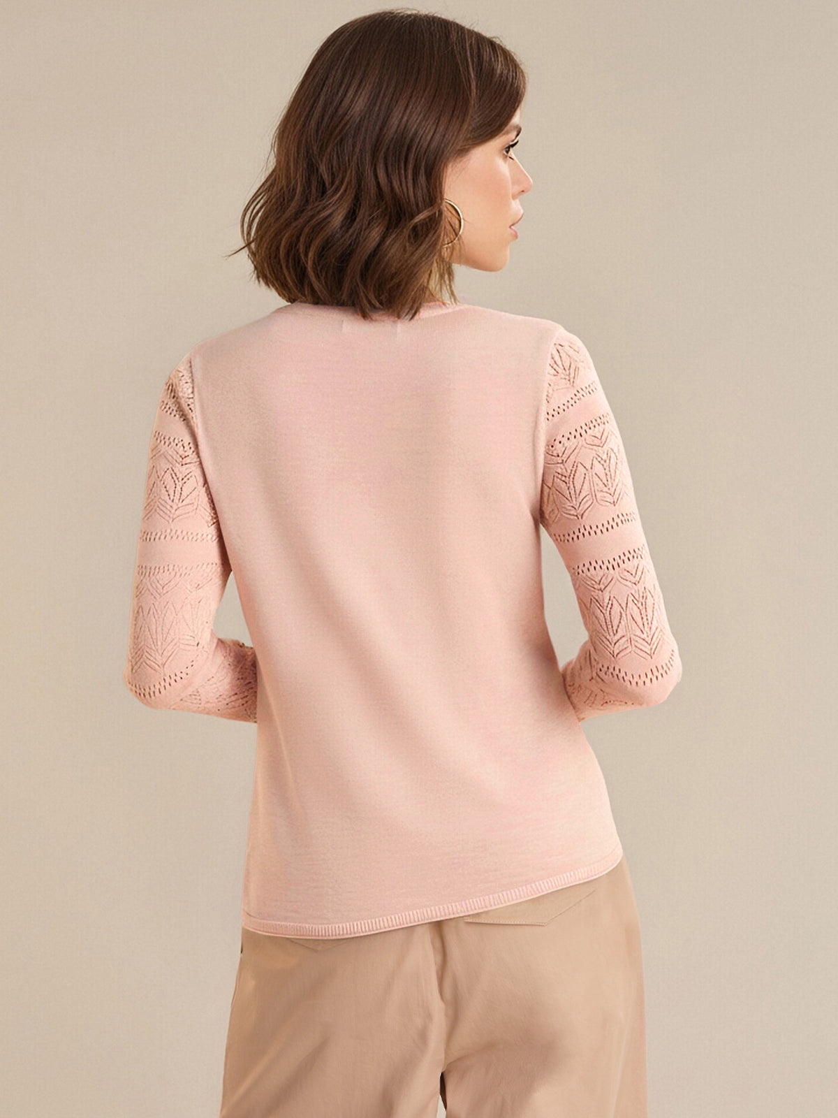 Woman wearing a light pink top with lace sleeves on a beige background