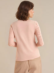 Woman wearing a light pink top with lace sleeves on a beige background