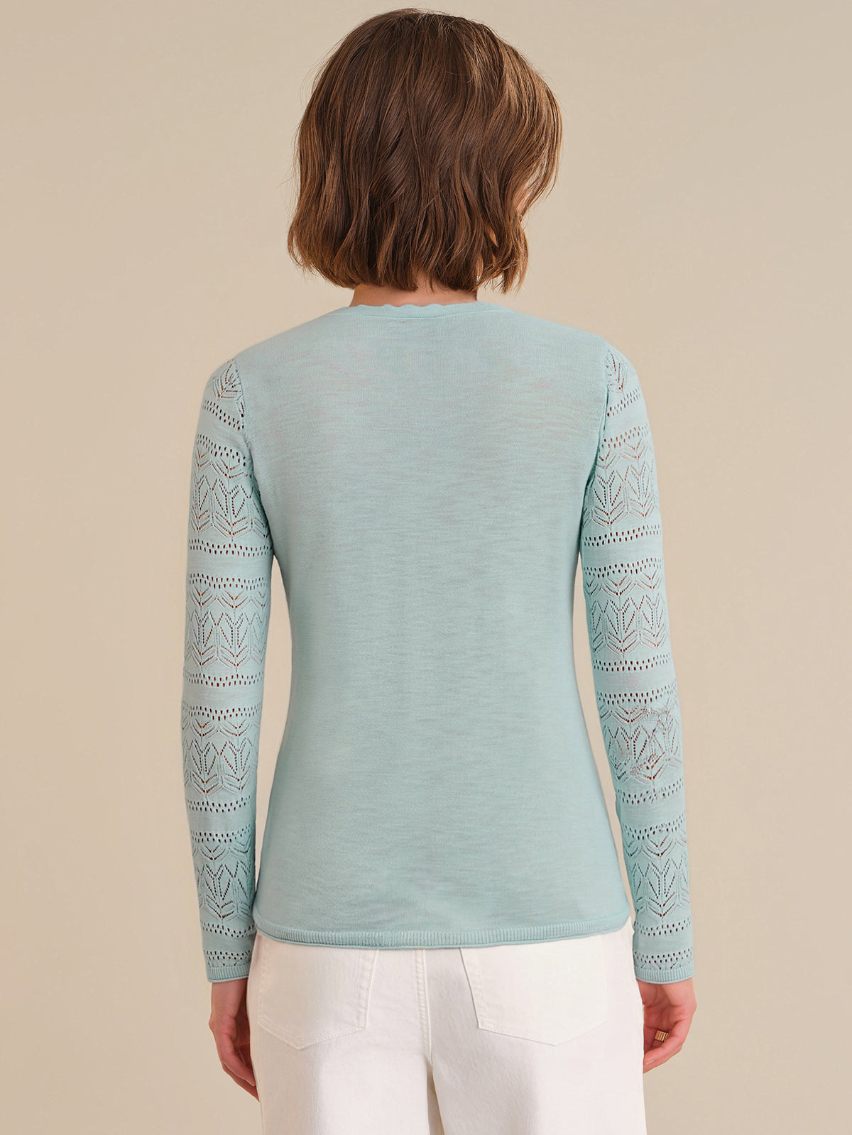 Person wearing a light blue long-sleeve top with lace details on a beige background