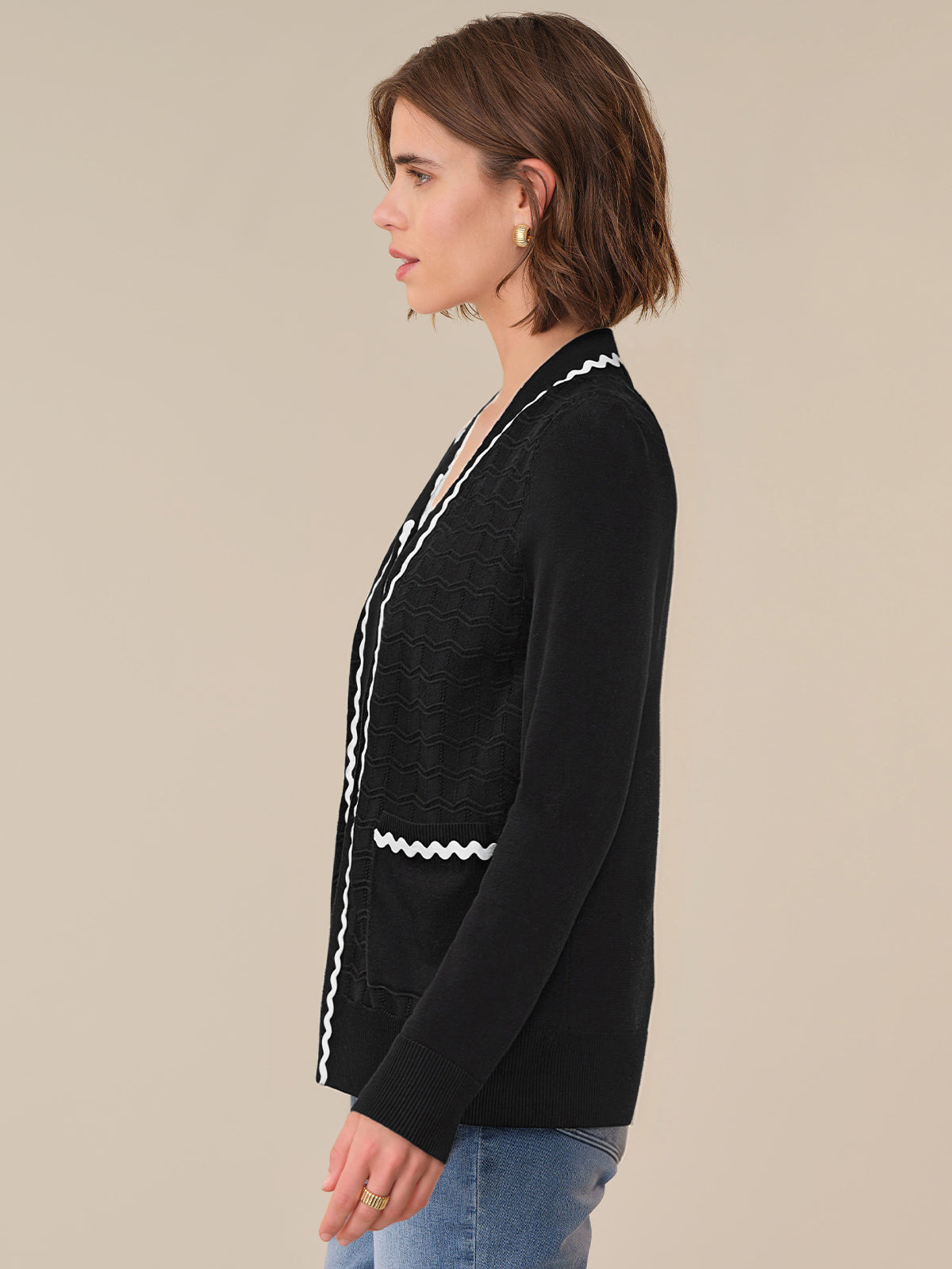 Woman wearing a black cardigan with white trim on a beige background