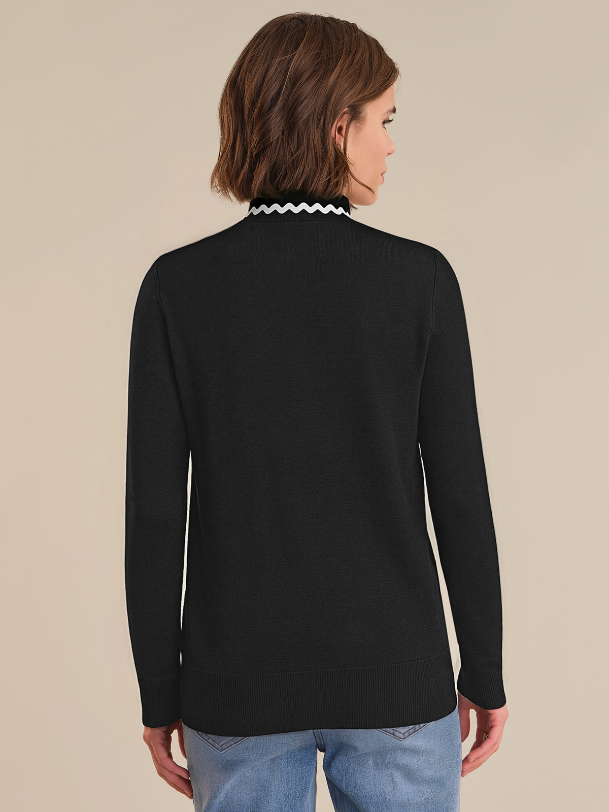 Person wearing a black long-sleeve top with a white collar against a beige background