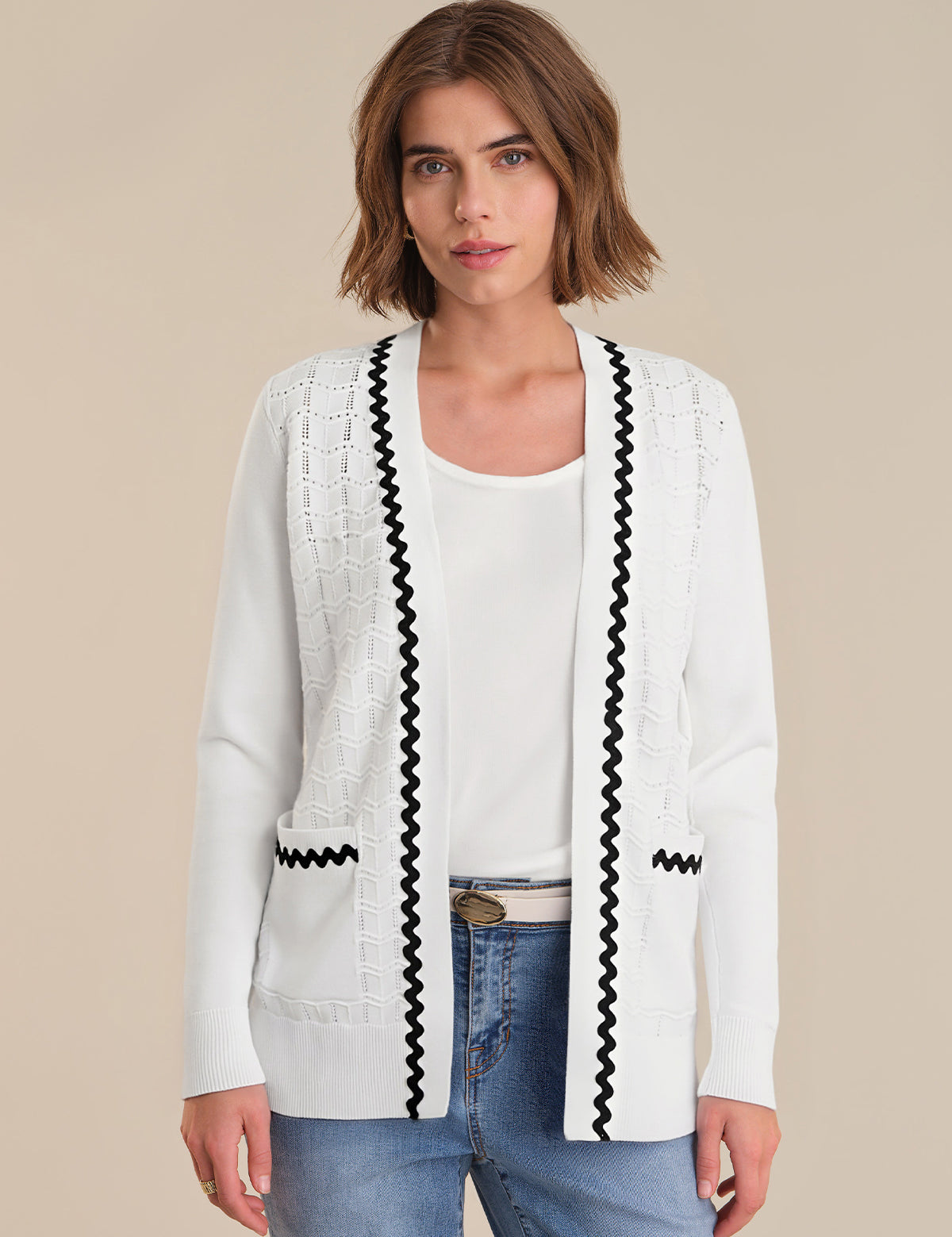 Woman wearing a white cardigan with black trim on a beige background