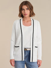 Woman wearing a white cardigan with black trim on a beige background
