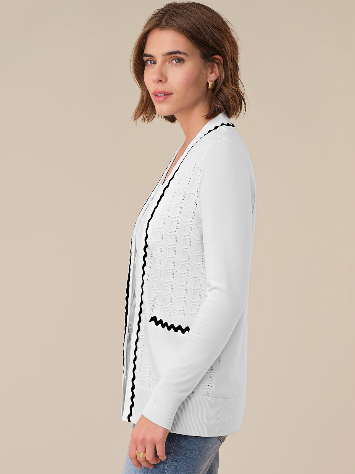 Woman wearing a white cardigan with black trim on a beige background
