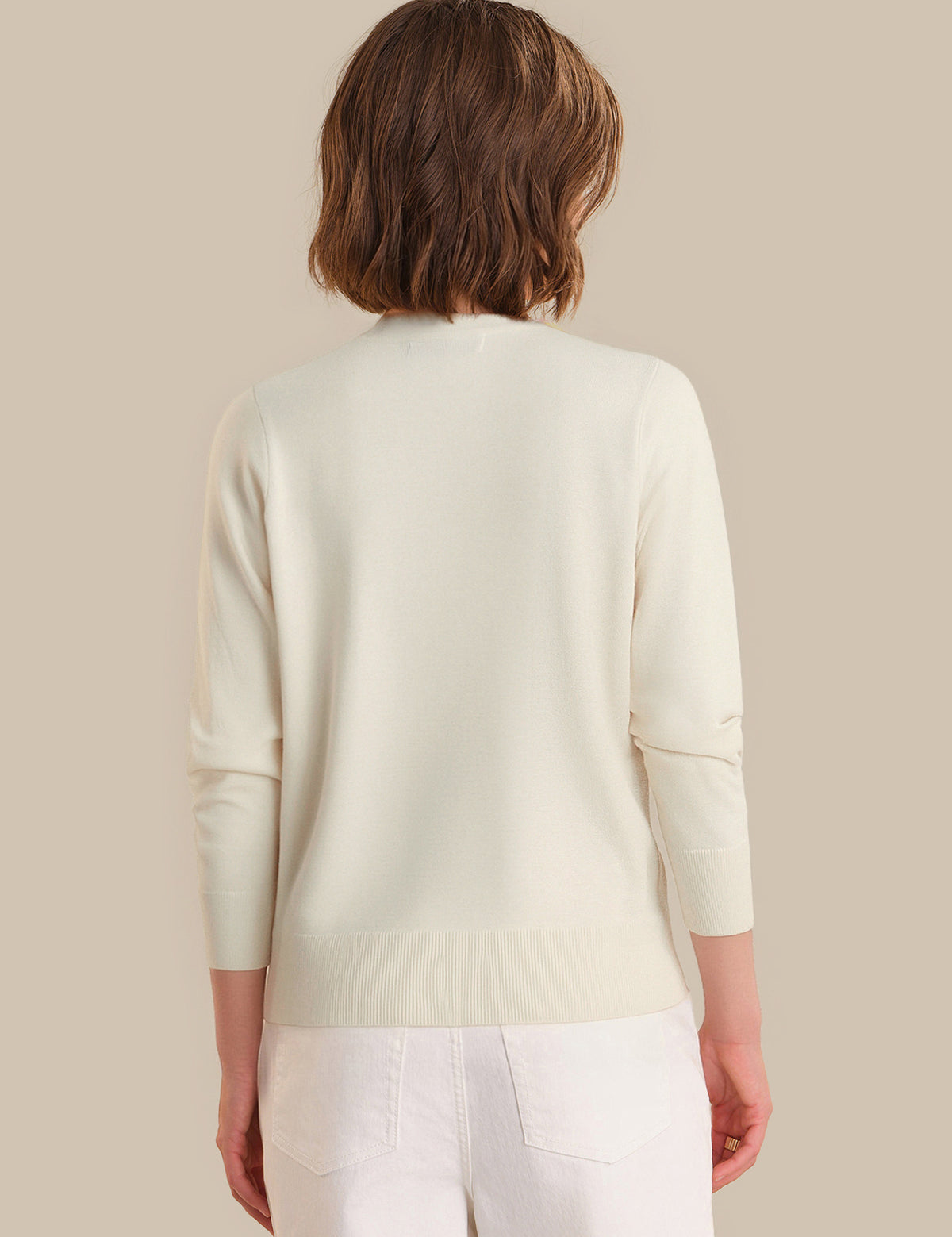 Person wearing a light green sweater and white pants on a beige background