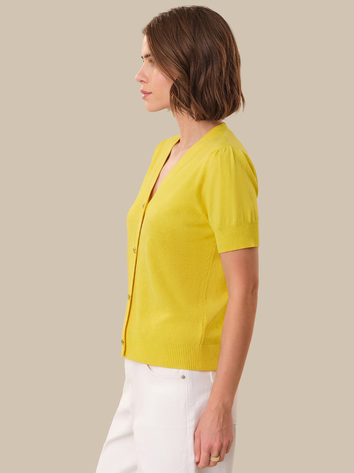 Woman wearing a yellow cardigan and white pants against a beige background