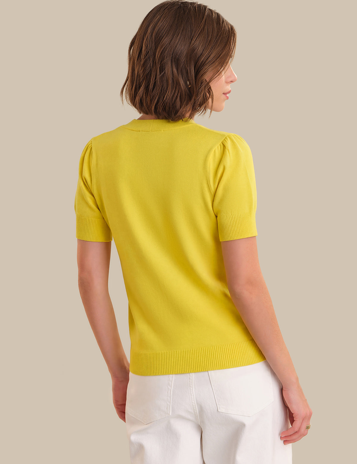 Woman wearing a yellow sweater and white pants against a beige background