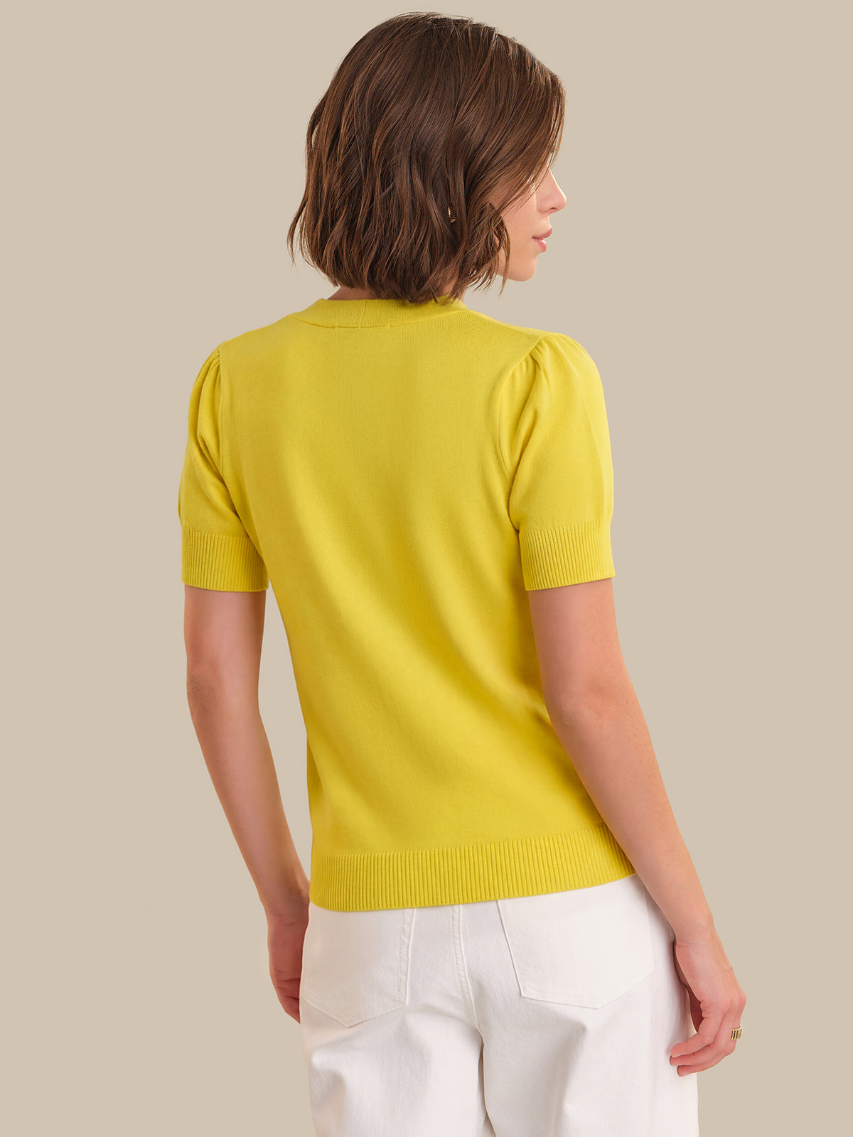 Woman wearing a yellow sweater and white pants against a beige background
