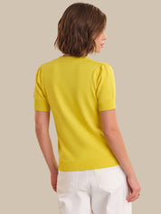 Woman wearing a yellow sweater and white pants against a beige background