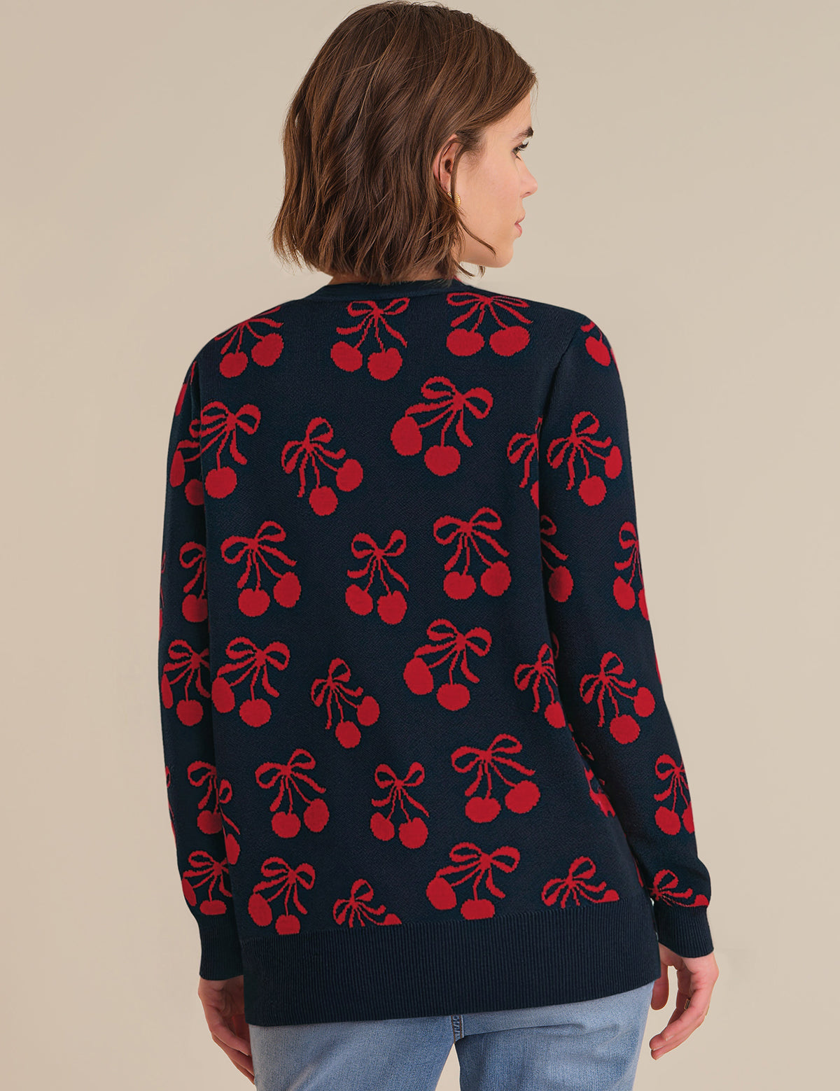 Person wearing a navy cardigan with red cherry and bow pattern on a beige background