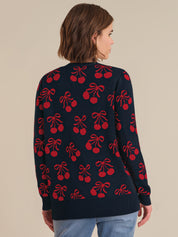 Person wearing a navy cardigan with red cherry and bow pattern on a beige background