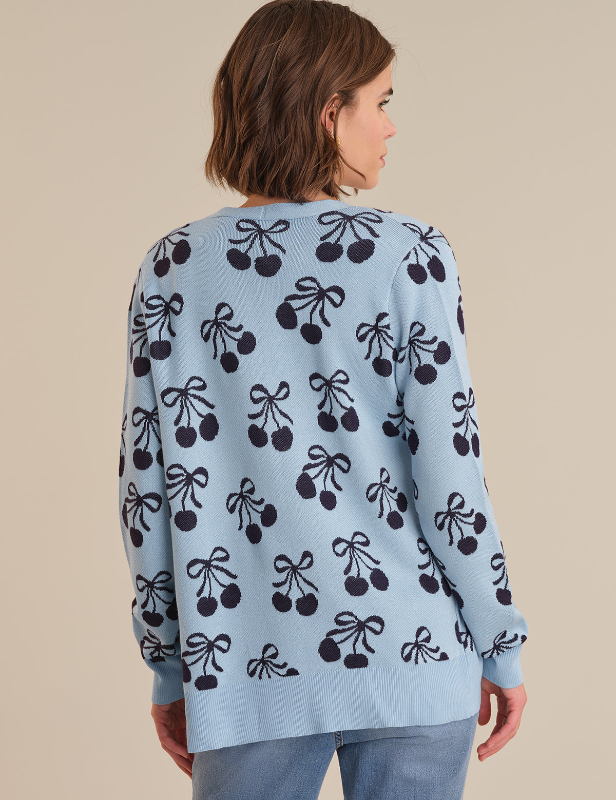 Woman wearing a light blue sweater with black cherry pattern on a beige background