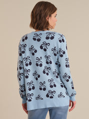 Woman wearing a light blue sweater with black cherry pattern on a beige background