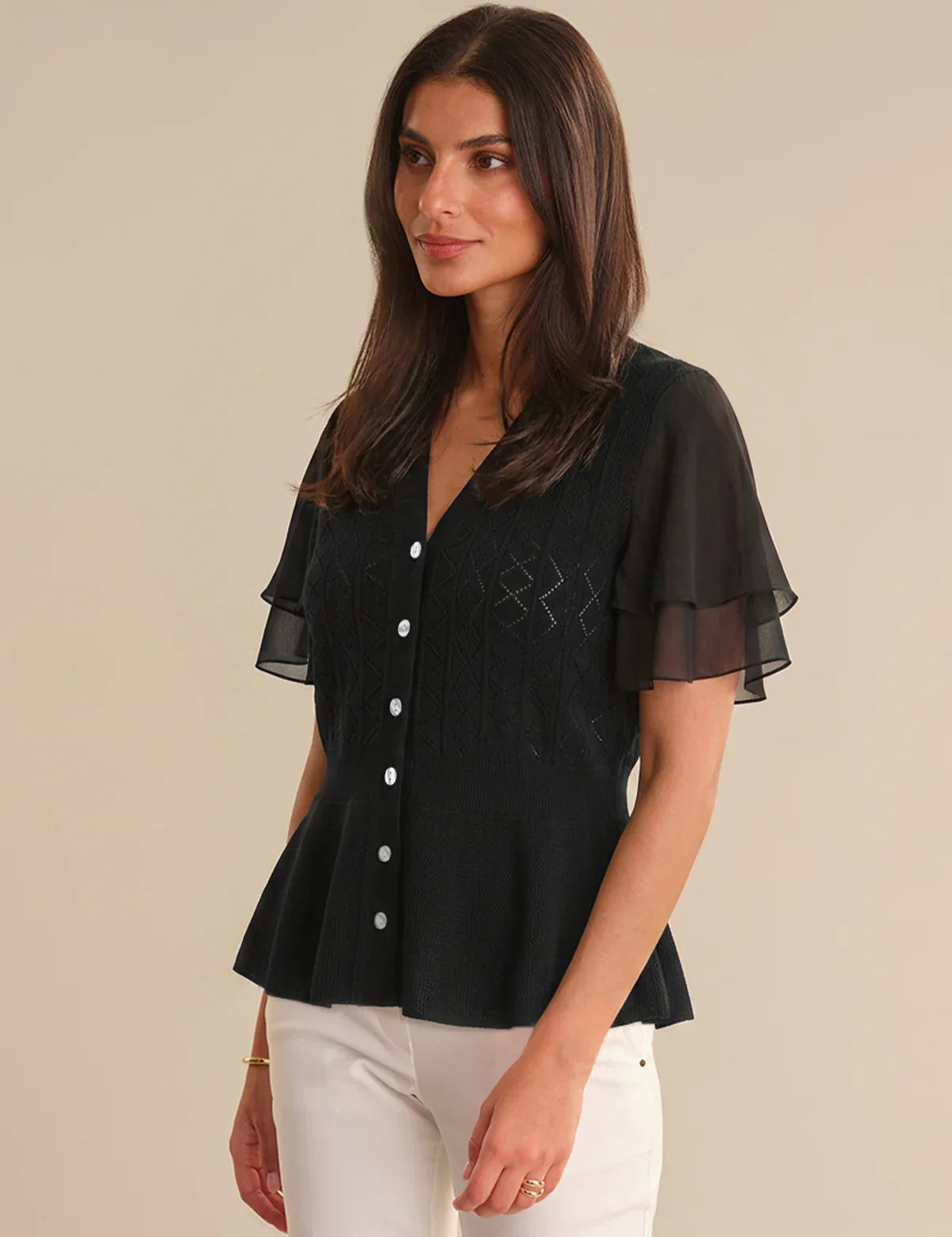 Woman wearing a black cardigan with sheer sleeves on a beige background