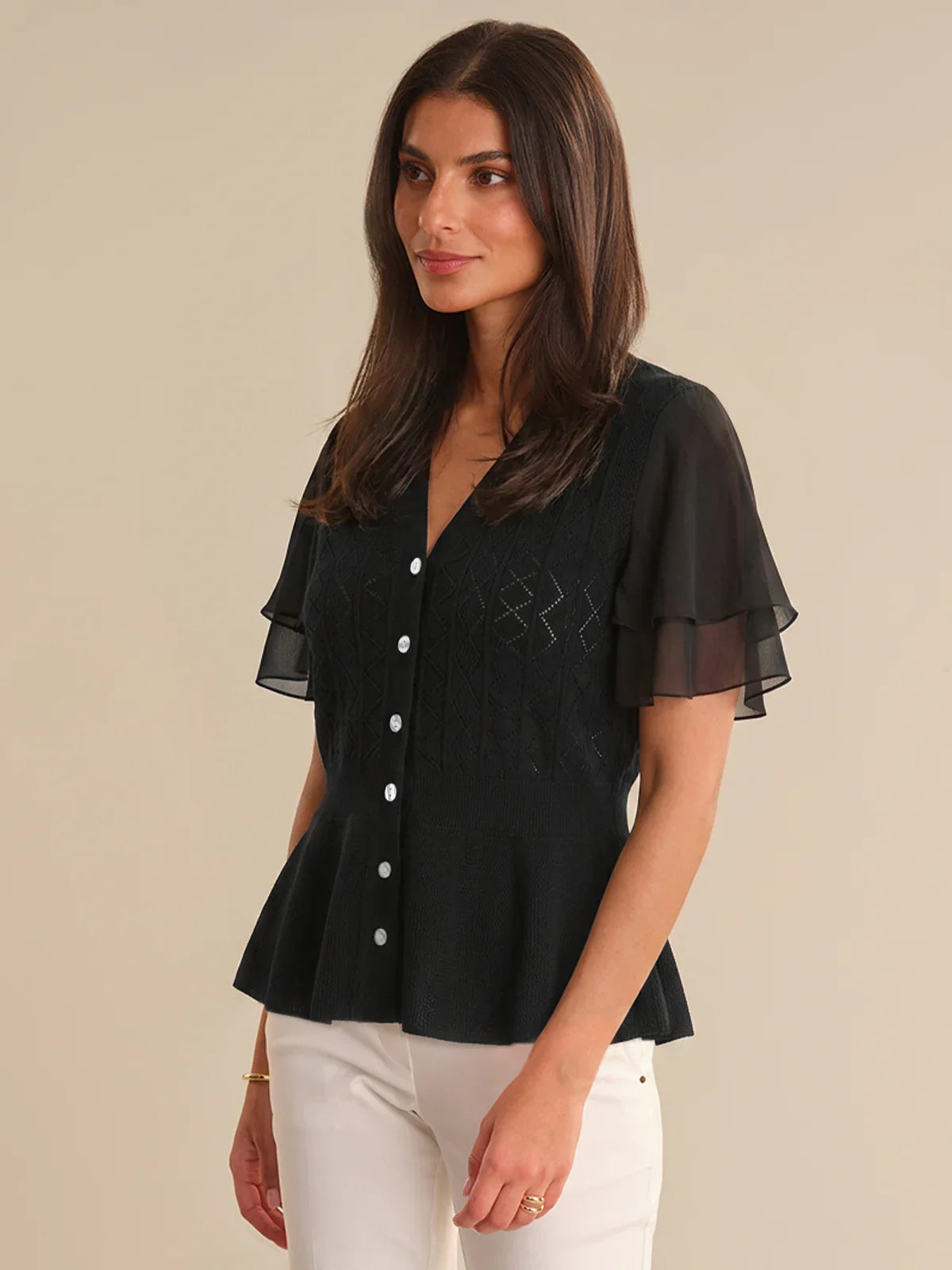 Woman wearing a black cardigan with sheer sleeves on a beige background