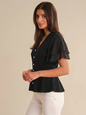 Woman wearing a black cardigan with ruffled sleeves on a beige background