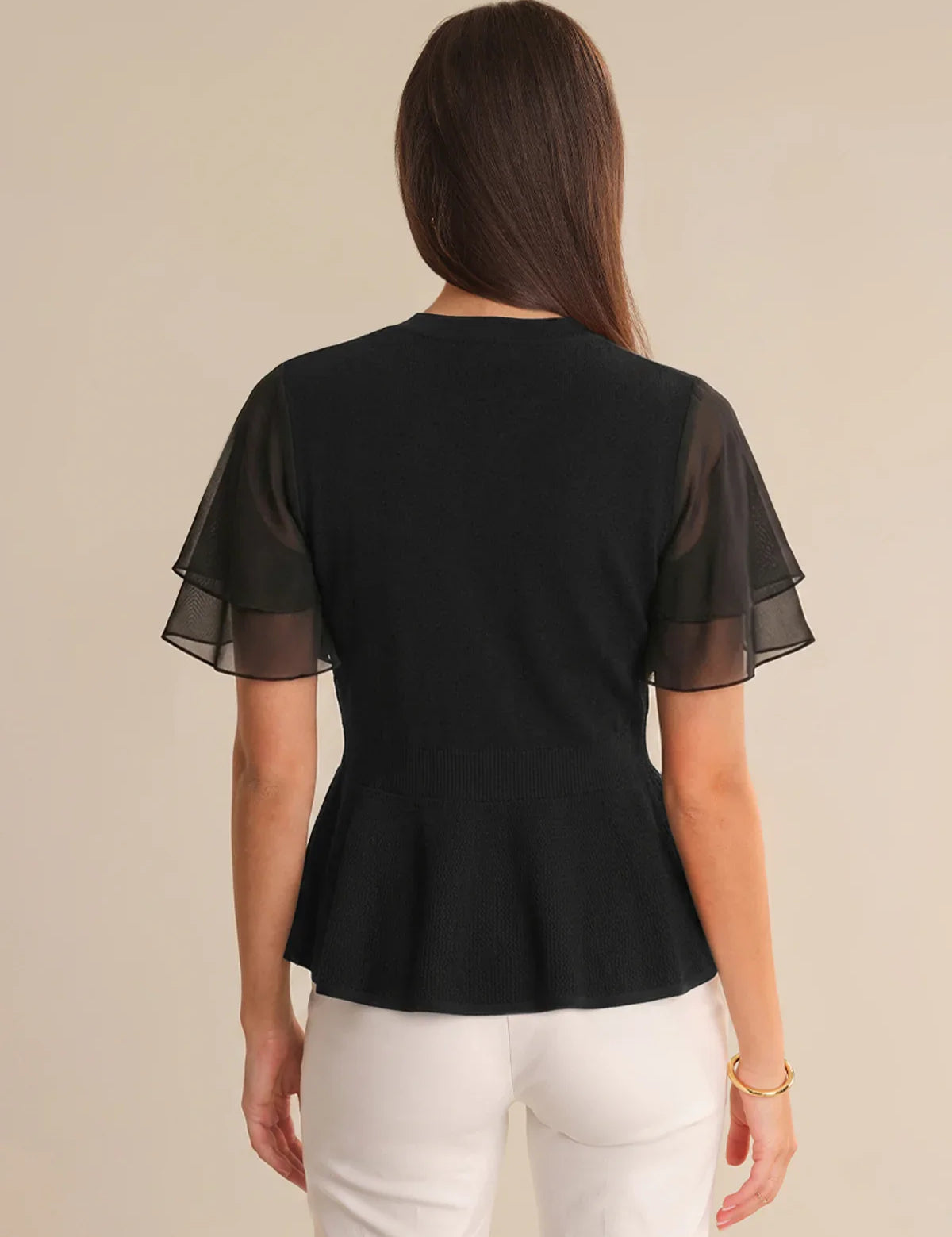 Woman wearing a black cardigan with sheer sleeves on a beige background